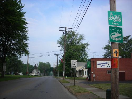 A quiet street scene with a café, trail signs, and a speed limit sign under a clear sky.
