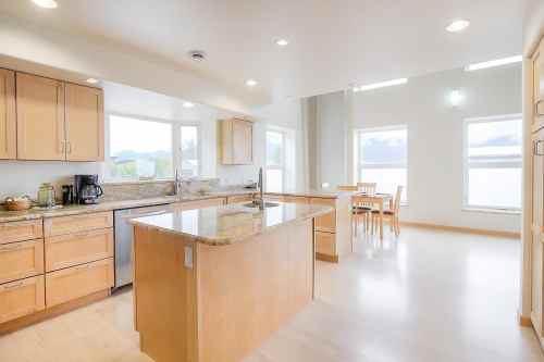 Bright, modern kitchen with wooden cabinets, granite countertops, and a dining area featuring a table and chairs by the windows.
