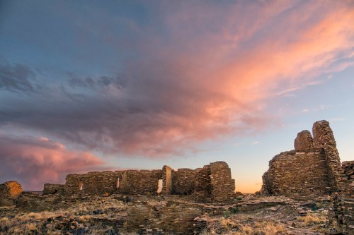 Ruins of an ancient stone structure against a colorful sunset sky with clouds.