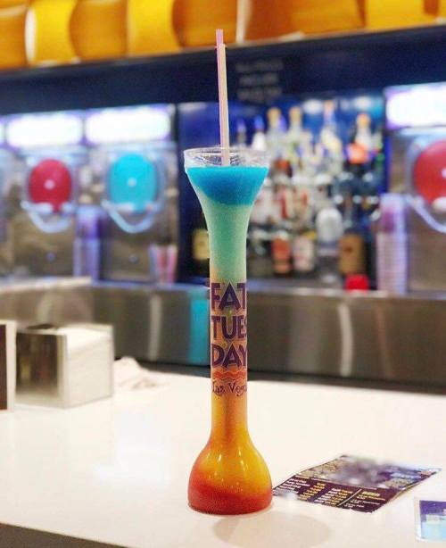 A tall, colorful cocktail in a unique glass with a straw, sitting on a bar counter.