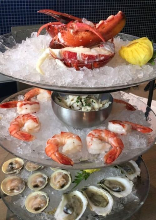 A tiered seafood platter featuring lobster, shrimp, crab, and oysters on ice, garnished with lemon and herbs.