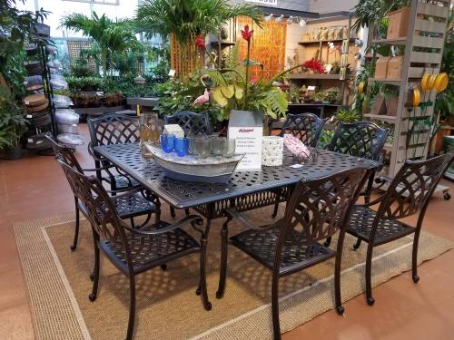 A metal patio dining set with eight chairs, surrounded by various plants and decorative items in a garden center.