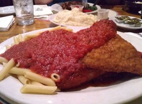 A plate of pasta topped with two pieces of breaded fish covered in marinara sauce, served with mashed potatoes.
