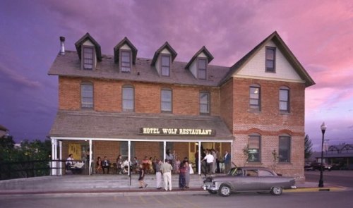 Historic Hotel Wolf Restaurant at dusk, featuring a brick facade, vintage car, and guests enjoying the outdoor seating.