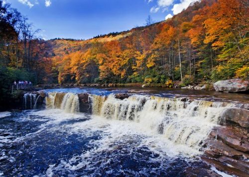 A scenic waterfall surrounded by vibrant autumn foliage and a clear blue sky.