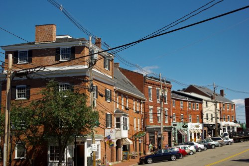A street view of brick buildings with shops and power lines under a clear blue sky.