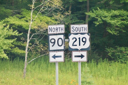 Road signs indicating directions for North 90 and South 219, surrounded by greenery.