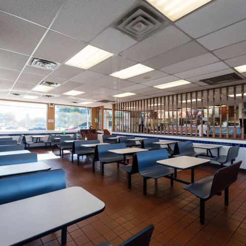 A spacious, empty diner with blue tables and chairs, featuring large windows and a counter in the background.