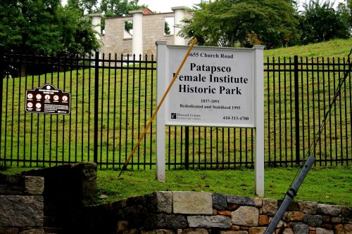 Sign for Patapsco Female Institute Historic Park, located on Church Road, with a green grassy area and a black fence.