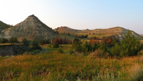A scenic landscape featuring rolling hills, grassy fields, and a clear sky at sunset.