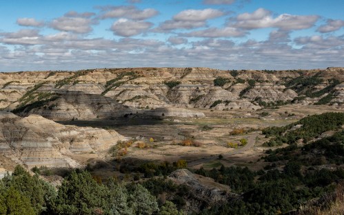 A panoramic view of layered hills and valleys under a cloudy sky, showcasing natural geological formations.