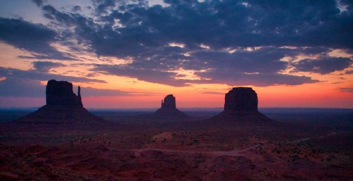 Sunset over Monument Valley, featuring iconic rock formations silhouetted against a colorful sky.
