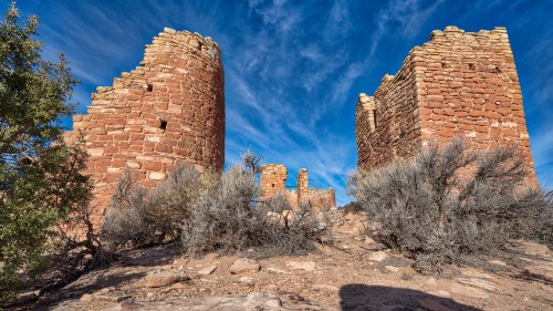 Ruins of ancient stone structures surrounded by sparse vegetation under a blue sky with scattered clouds.