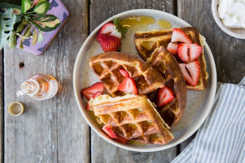 A plate of golden waffles topped with fresh strawberries and drizzled with syrup, set on a rustic wooden table.