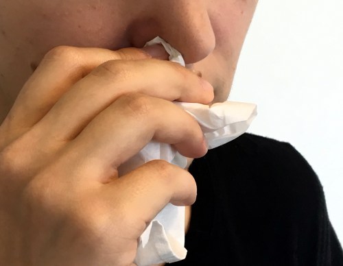 A close-up of a person holding a tissue to their nose, appearing to be in discomfort or sneezing.