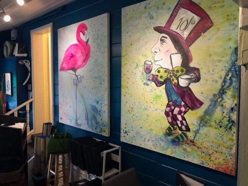 Two colorful paintings on a blue wall: one of a flamingo and the other of a whimsical character in a top hat.