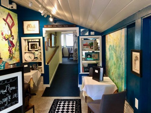 A cozy restaurant interior with colorful artwork, tables set for dining, and a welcoming hallway leading to more seating.