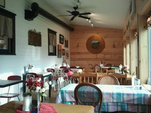 Cozy restaurant interior with wooden walls, tables set with checkered tablecloths, and decorative flowers.