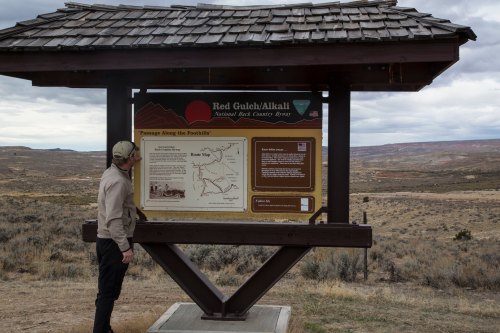 A person stands by an informational sign at Red Gulch/Alkali, overlooking a vast, arid landscape.