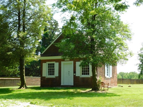 A small brick house surrounded by trees, with white shutters and a grassy area in front.