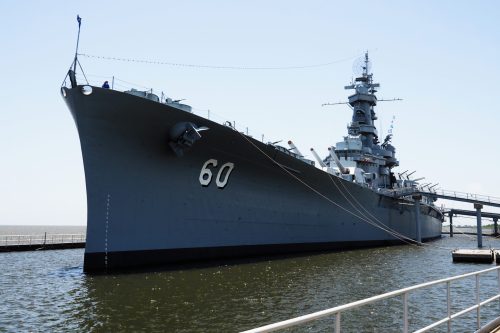 A large naval ship docked at a pier, with the number 60 displayed on its bow against a clear blue sky.
