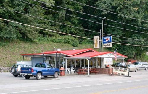 A small diner with a red roof, outdoor seating, and a Pepsi sign, surrounded by trees and parked cars.
