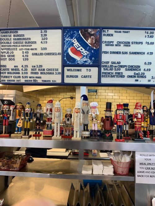 A menu board at Burger Carte with various food items and prices, featuring nutcracker figurines on display below.