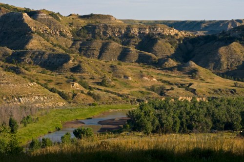 A winding river flows through rolling hills and lush greenery under a clear sky.