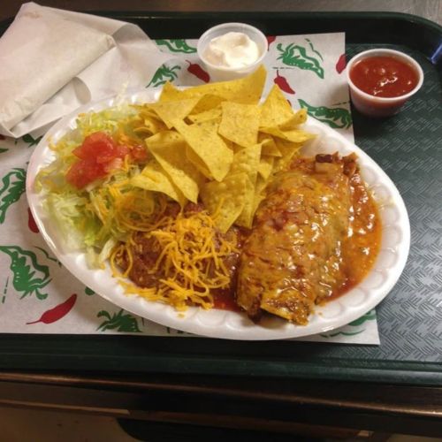 A plate of enchiladas topped with cheese, served with lettuce, tomatoes, tortilla chips, and a side of salsa and sour cream.