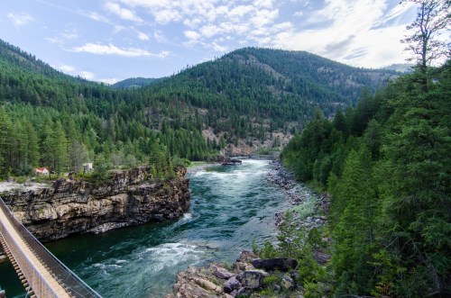 A scenic view of a river winding through lush green mountains, with a bridge crossing over rocky terrain.