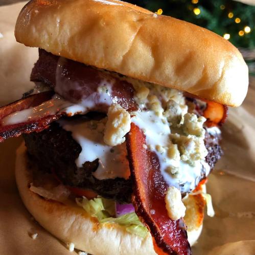 A close-up of a juicy burger topped with bacon, blue cheese, and creamy sauce, served on a soft bun.