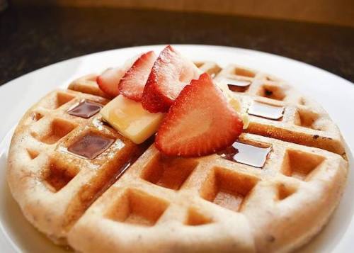 A plate of waffles topped with sliced strawberries and butter, drizzled with syrup.
