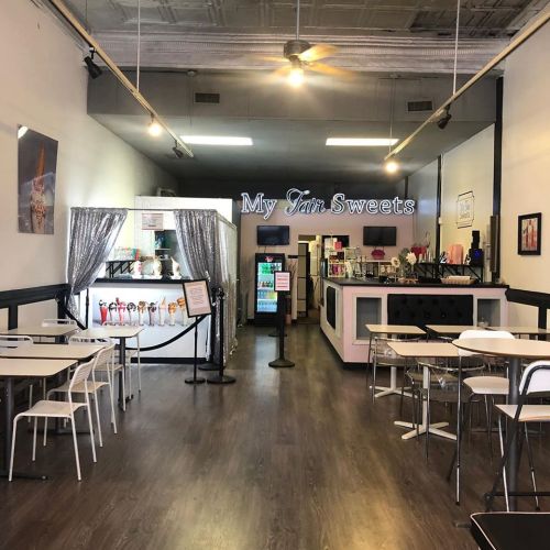 Interior of a dessert shop named "My Fair Sweets," featuring tables, a service counter, and colorful decor.