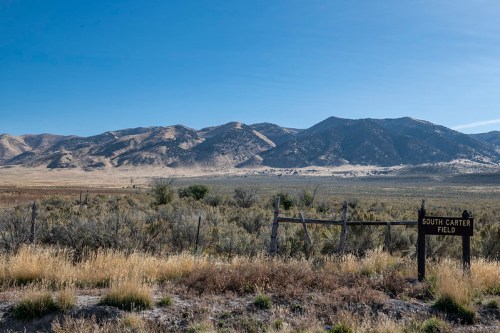 A vast landscape featuring mountains in the background, a grassy field, and a sign for "South Carter Field."