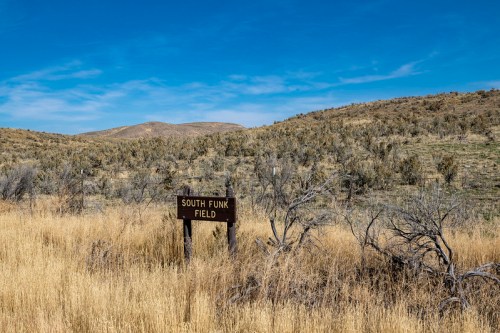 A sign for South Funk Field stands in a grassy area with rolling hills and a blue sky in the background.
