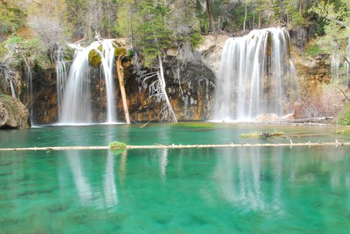 Two waterfalls cascade into a clear turquoise pool, surrounded by lush greenery and rocky cliffs.