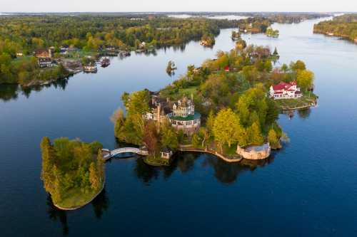 Aerial view of a lush green island with homes, surrounded by calm blue waters and trees in a scenic landscape.