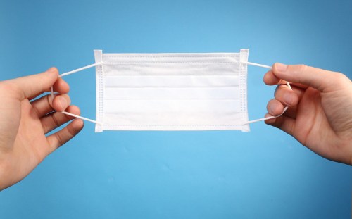 A pair of hands holding a white surgical mask against a blue background.