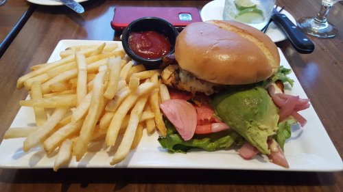 A plate with a burger topped with lettuce, tomato, and avocado, served with fries and a small bowl of ketchup.