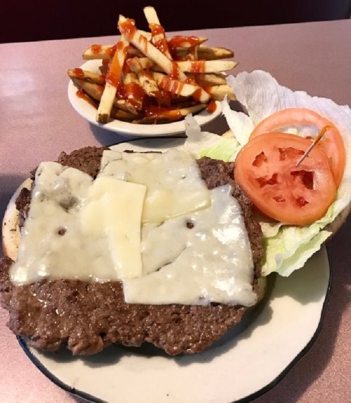 A plate with a cheeseburger topped with melted cheese, lettuce, and tomato, alongside a serving of fries with ketchup.