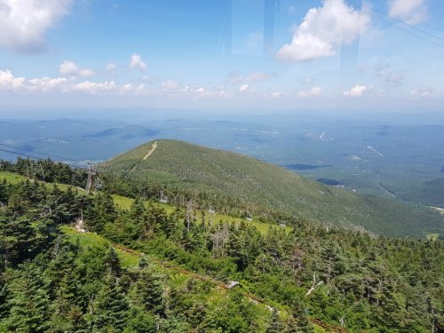 A panoramic view of a green mountain landscape under a blue sky with scattered clouds.