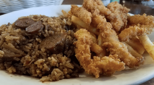 A plate featuring seasoned rice with sausage and crispy fried chicken strips alongside golden French fries.