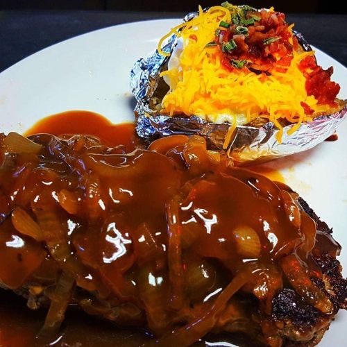 A plate featuring a meatloaf topped with onion gravy and a baked potato with cheese, bacon, and chives.