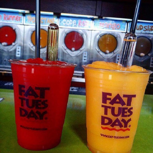 Two colorful frozen drinks in clear cups with straws, one red and one yellow, on a vibrant green counter.