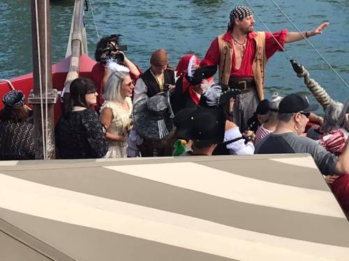 A group of people in pirate costumes on a boat, with one person gesturing and others enjoying the scene.