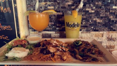 A colorful plate of Mexican food with rice, grilled chicken, sautéed vegetables, and drinks on the side.