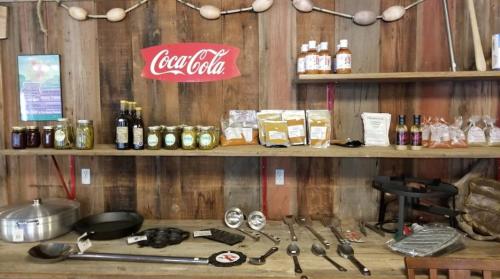 A rustic wooden shelf displays jars, spices, and cooking tools, with a Coca-Cola sign above.