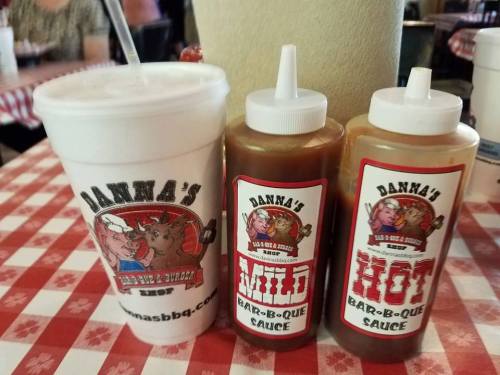 A cup and two squeeze bottles of barbecue sauce labeled "Mild" and "Hot" on a checkered tablecloth.
