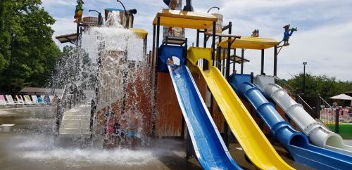 Colorful water slides at a splash park, with water cascading down and children playing in the pool below.