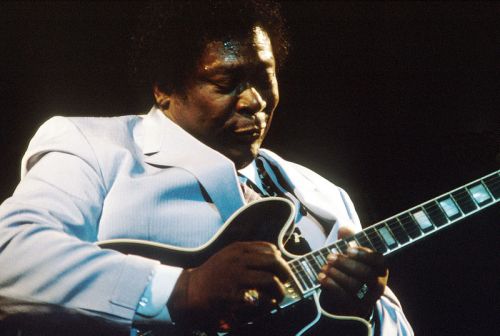 A musician in a light suit plays an electric guitar, focused and immersed in the music.